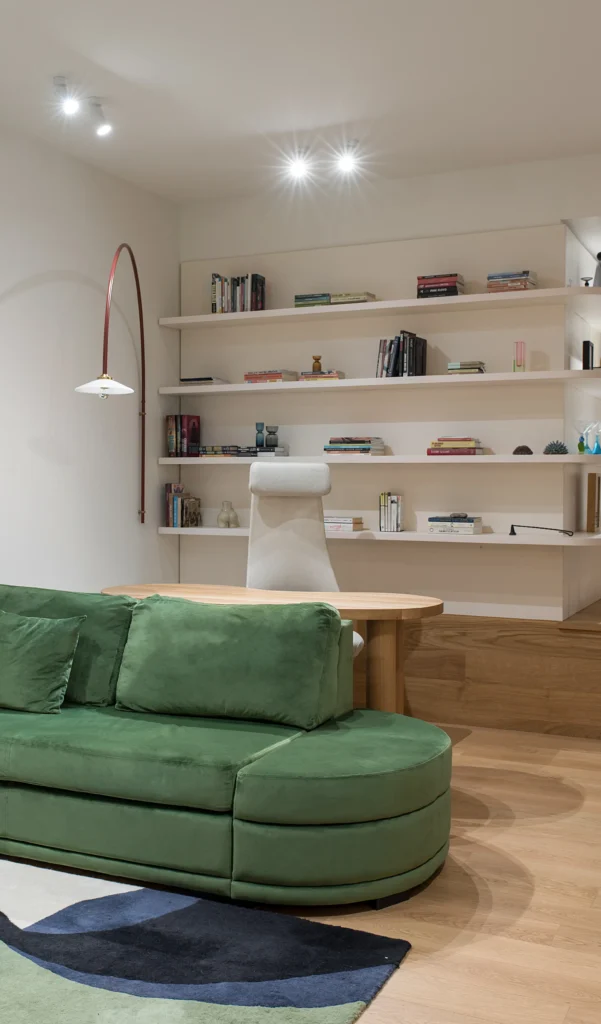 Living cu canapea verde curbată, rafturi deschise cu obiecte personale și lampadar arcuit
