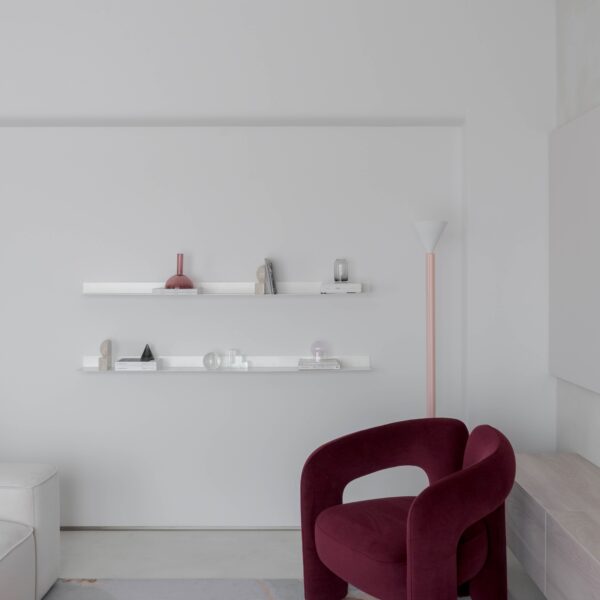 Living cu fotoliu burgundy Cassina Dudet, rafturi albe și accente pastelate într-un apartament minimalist glam