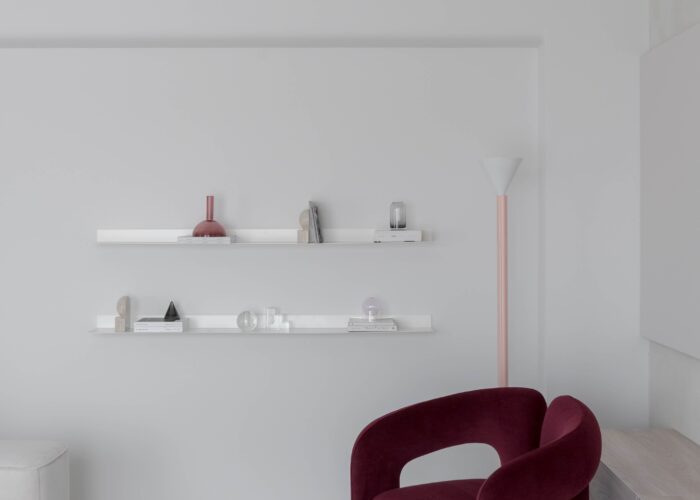 Living cu fotoliu burgundy Cassina Dudet, rafturi albe și accente pastelate într-un apartament minimalist glam